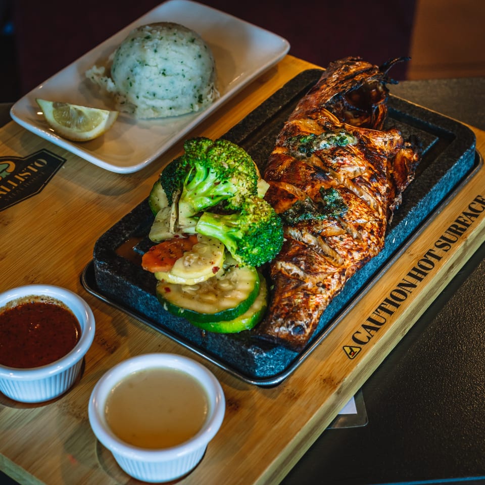 Grilled fish with broccoli, zucchini, and carrots, served with mashed potatoes and two dipping sauces.