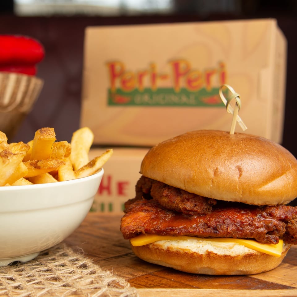 Peri Peri Original chicken sandwich with cheese and fries, with a branded box in the background.
