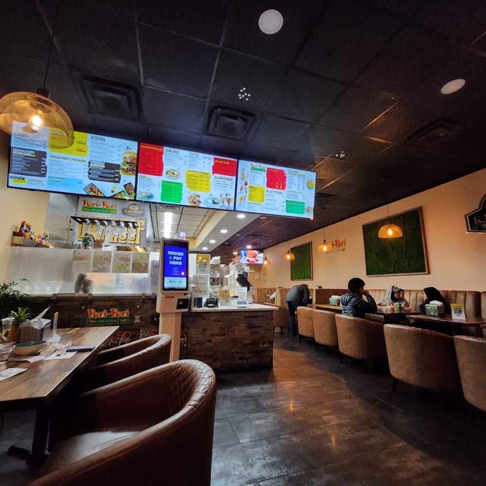 Interior of Peri Peri Original & Kallisto Steakhouse with menu boards, order kiosk, and customers dining.